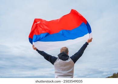 Seorang pemuda memegang bendera Rusia di langit, tampak belakang