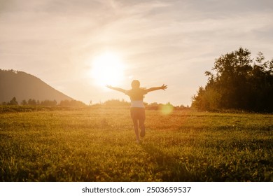 Cô bé hạnh phúc chạy trên nền núi và bầu trời trong cảnh hoàng hôn mùa hè tuyệt đẹp. Đứa trẻ chạy với hai tay giơ lên ​​như cánh máy bay, kỳ nghỉ mơ ước thời thơ ấu. Giấc mơ của trẻ em, phi công máy bay