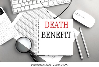 Notebook with the words DEATH BENEFIT on desk with a keyboard, calculator, pen, and charts .