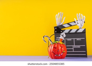 Horror movie, series night, Halloween cinema party with trick-or-treating sweets bucket, popcorn, movie clapperboard and Halloween decorations on high-colored background copy space