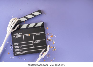 Horror movie, series night, Halloween cinema party with trick-or-treating sweets bucket, popcorn, movie clapperboard and Halloween decorations on high-colored background copy space