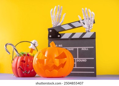 Horror movie, series night, Halloween cinema party with trick-or-treating sweets bucket, popcorn, movie clapperboard and Halloween decorations on high-colored background copy space