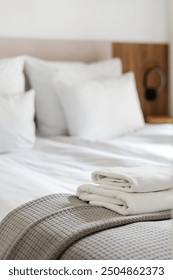 Vertical shot of a neatly arranged bed features soft pillows and a cozy gray blanket with white folded towels. Concepts of hotel suite, room service and hospitality
