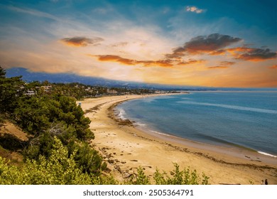 landskap musim panas yang indah di pantai dengan tebing coklat yang dilitupi pokok dan tumbuhan hijau yang subur dan air laut biru dalam, awan kuat pada waktu matahari terbenam di pantai Leadbetter di Santa Barbara California