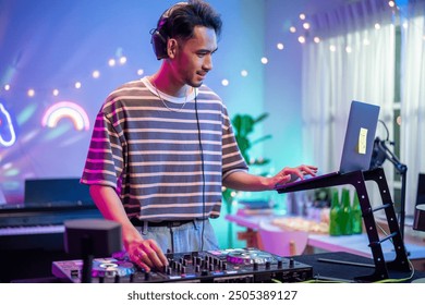 Artista DJ asiático joven mezclando y haciendo scratch con el controlador de la mesa de mezclas. Músico DJ atractivo divirtiéndose mezclando música en la consola tocando botones y tocando música electrónica en una fiesta de neón.