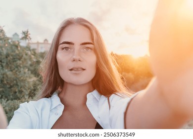 Amber Golden Hour Nga afër një grua e larë në dritën e orës së artë duke bërë selfie në perëndimin e diellit në parkun veror. Turisti i lumtur kënaqet duke bërë foto selfie jashtë për kujtime