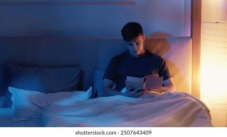 Peaceful man enjoying reading book in bed with warm soft lighting in intimate bedroom setting.