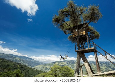 Ekvador, Baños'taki La Casa del Árbol'da ünlü "Dünyanın Sonundaki Salıncak"ın keyfini çıkaran bir kişiyi yakalayan canlı ve dinamik bir fotoğraf. Yüksek bir ağaç eve bağlı salıncak.