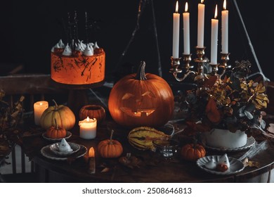 Décoration de table élégante et magnifique pour une fête d'Halloween. Bougies allumées dans un lustre vintage, gâteau fait main avec des fantômes en meringue, citrouille faite main. Fond sombre, vieux meubles en bois, toile d'araignée