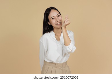 Uma mulher alegre com uma blusa branca fazendo um gesto de coração com os dedos, expressando amor ou afeição contra um fundo bege