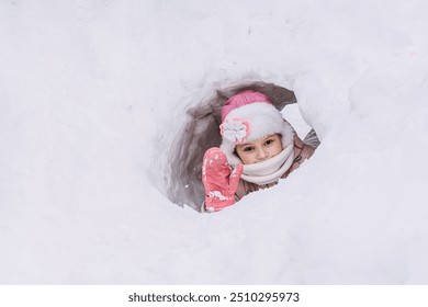 A little girl is playing in the snow outside in the park, snowball games, sculpting a castle out of snow, games in the snow, climate change, happy moments outdoors. Winter Vacation.