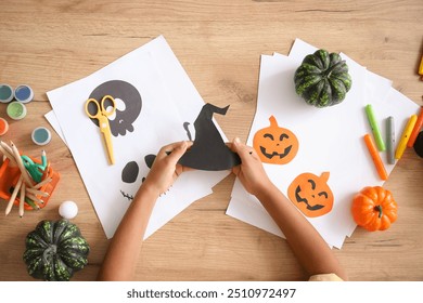 Adolescente com chapéu de bruxa de papel fazendo decorações de Halloween na mesa, vista de cima