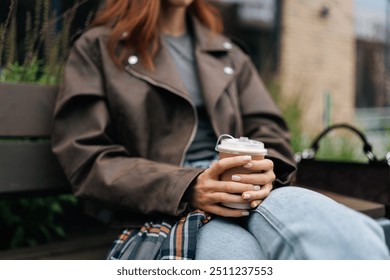 Closeup gecroppet Schéiss vun enger entspaanter Fra genéisst waarme Kaffi dobaussen um bewölktem Hierschtdag, hëlt Paus vum urbane Liewen fir mat gemittleche Gedrénks ze relaxen. Zoumaache vu weiblech genéisst Kaffi op der Parkbänk.