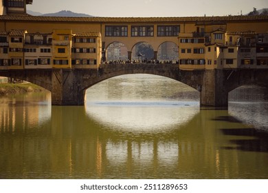 View of the historic Ponte Vecchio bridge reflecting on the Arno River in Florence, Italy, during sunset.