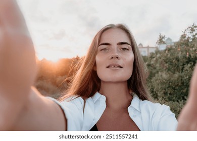 Amber Golden Hour Nga afër një grua e larë në dritën e orës së artë duke bërë selfie në perëndimin e diellit në parkun veror. Turisti i lumtur kënaqet duke bërë foto selfie jashtë për kujtime
