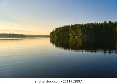 Lac en Suède au lever du soleil avec une lumière romantique, de l'eau bleue et des arbres sur la rive. La nature scandinave au nord