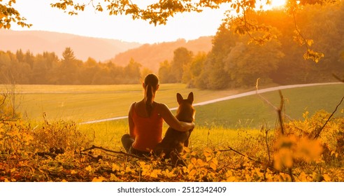 SILHOUETTE, LENS FLARE: Wanita muda dan anjingnya berkongsi detik damai menonton matahari terbenam. Momen persahabatan yang tulen antara pemilik anjing dan haiwan peliharaannya di tengah-tengah persekitaran semula jadi yang damai.