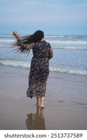 A serene scene at Puri Beach, Odisha, India. It shows a woman with long flowing hair wearing a floral-patterned dress, walking barefoot along the shoreline.
