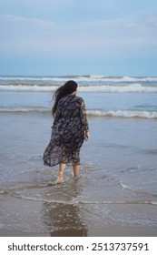 A serene scene at Puri Beach, Odisha, India. It shows a woman with long flowing hair wearing a floral-patterned dress, walking barefoot along the shoreline.