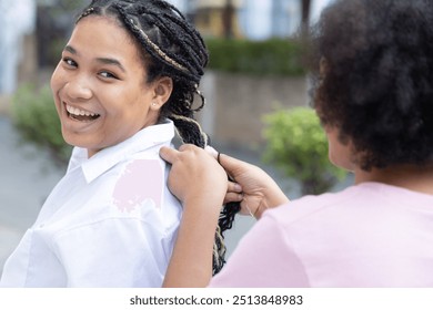 Des amis africains souriants et heureux, une jeune femme africaine aide à coiffer son amie ou sa sœur afro, coiffure afro tressée