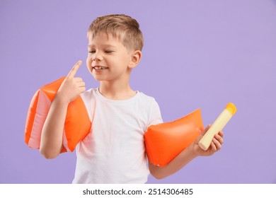 Anak laki-laki kecil yang lucu dengan krim tabir surya dan ban renang di latar belakang ungu