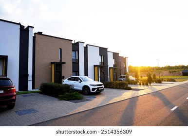 Konut alanında modern şehir evleri. Yeşil ortamda yeni apartman binaları. Yeşil çimli kaldırım boyunca şehir evi bulunan sokak. Evdeki otoparkta araba. Banliyöde şehir evi.