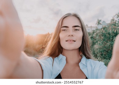 Amber Golden Hour Nga afër një grua e larë në dritën e orës së artë duke bërë selfie në perëndimin e diellit në parkun veror. Turisti i lumtur kënaqet duke bërë foto selfie jashtë për kujtime
