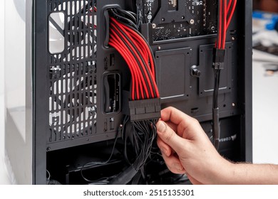 一只手将黑色 ATX 电源线连接到光滑黑色机箱内的华硕主板。主板在黑色 PCB 上带有红色装饰，并配有钢化玻璃侧板，便于查看。