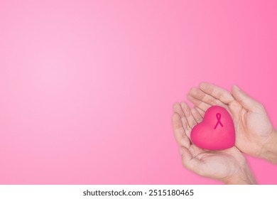 Mâinile care țin o inimă roz cu o panglică de cancer de sân pe un fundal roz. Simbolizează dragostea, îngrijirea și sprijinul pentru conștientizarea cancerului de sân. Campanii octombrie Pink și inițiative pentru sănătatea femeilor