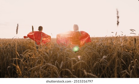 Bambini felici in mantello rosso da supereroe che corrono alla luce del sole campo di grano secco vista posteriore. Bambina e bambino allegri che giocano eroe volante fantasia immaginazione sognando gioco giocando godere libertà e infanzia