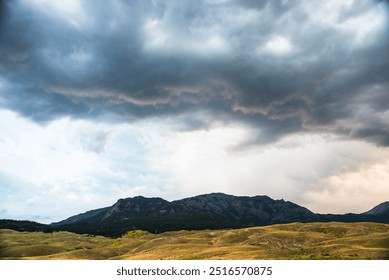 Tamni, dramatični oblaci skupljaju se iznad valovitih brda i udaljenih planina.