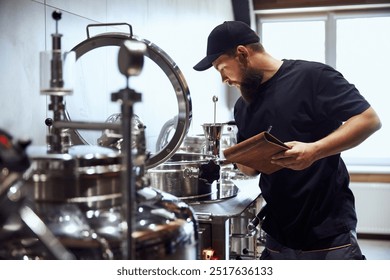Szakállas férfi, technológus sörfőző eszközöket ellenőrzi, jegyzeteket készít, bemutatja a sörkészítéshez szükséges szakértelmet. Sör, sörfőzde, gyártás, minőség-ellenőrzés fogalma