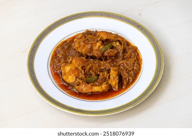 Tasty Rui fish curry or Rui mach bhuna in a white plate on a light wooden surface. Traditional Bengali food.