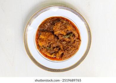 Tasty Rui fish curry or Rui mach bhuna in a white plate on a light wooden surface. Traditional Bengali food. Top view.