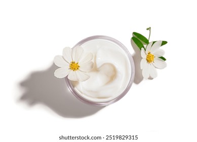 Cosmetic cream jar with delicate white flowers isolated on white background, top view. Dermatologic calming cream in opened jar, organic natural skin care.