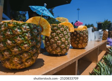 Scena all'aperto con ananas svuotati, usati come contenitori per bevande, guarniti con fette d'arancia e colorati ombrellini da cocktail, ambientata a Lisbona, Portogallo.