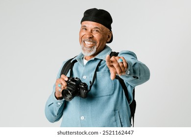Fotógrafo idoso feliz com uma câmera em pé contra um fundo branco. Homem idoso alegre apontando para a câmera. Fotógrafo idoso viajando e tirando fotos de momentos alegres.