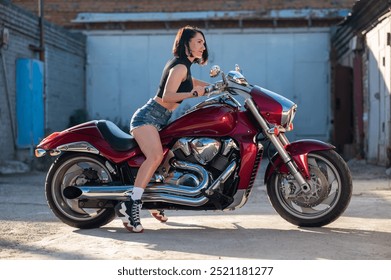 Wanita berambut coklat mengenakan celana pendek di atas sepeda motor merah.
