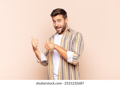 young man smiling cheerfully and casually pointing to copy space on the side, feeling happy and satisfied