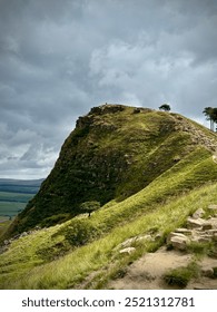 Scenic landscape of the Peak District National Park in England, featuring rolling hills, rugged rock formations, and lush green valleys under a clear blue sky. A panoramic view