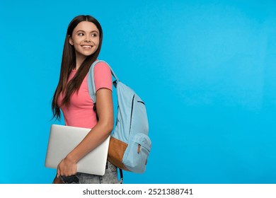 Atraktivní usměvavá dívka středoškolská studentka studentka v neformálním oblečení s batohem držícím notebook, chodící do školy s počítačovým kopírovacím prostorem izolovaným na modrém pozadí