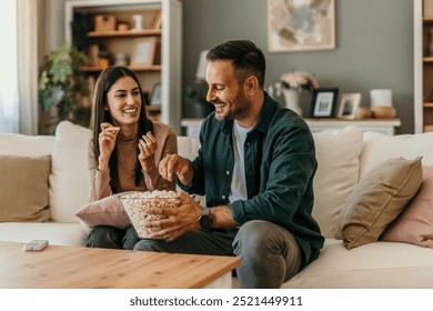 Una pareja de enamorados en casa pasan un día relajado juntos. Están viendo la televisión y comiendo palomitas de maíz.