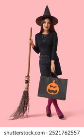 Gyönyörű fiatal boldog ázsiai nő öltözött boszorkány Halloween bevásárló táska és varázsseprű rózsaszín háttér