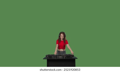Stüdyoda yeşil ekranlı kroma anahtarı bulunan DJ masasında kırmızı tişört giyen genç bir kadın DJ performans sergiliyor