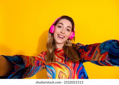 Selfie of youth model blonde girl wearing bright pink earphones chilling walking alone enjoying music isolated on yellow color background