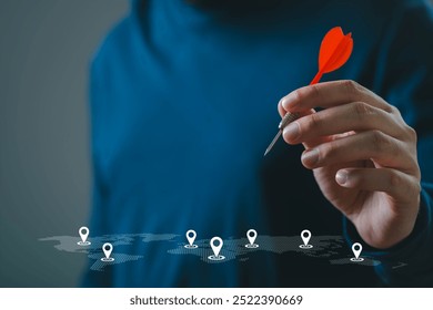 Hand holding dart targeting locations on digital map. Concept of strategy, planning, and goal setting in business and travel.