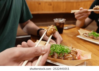 Seorang lelaki sedang mengambil bola takoyaki dengan penyepitnya di bar bersama rakan-rakan. Makanan jalanan yang popular di Osaka, Jepun
