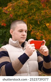 20-year-old positive guy is looking at the smartphone screen in a red case, playing a game, watching a video or contacting online. wireless technologies.