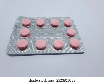 One sheet of red and pink tablet medicine contains ten pieces isolated on a gray background