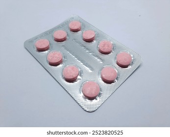 One sheet of red and pink tablet medicine contains ten pieces isolated on a gray background